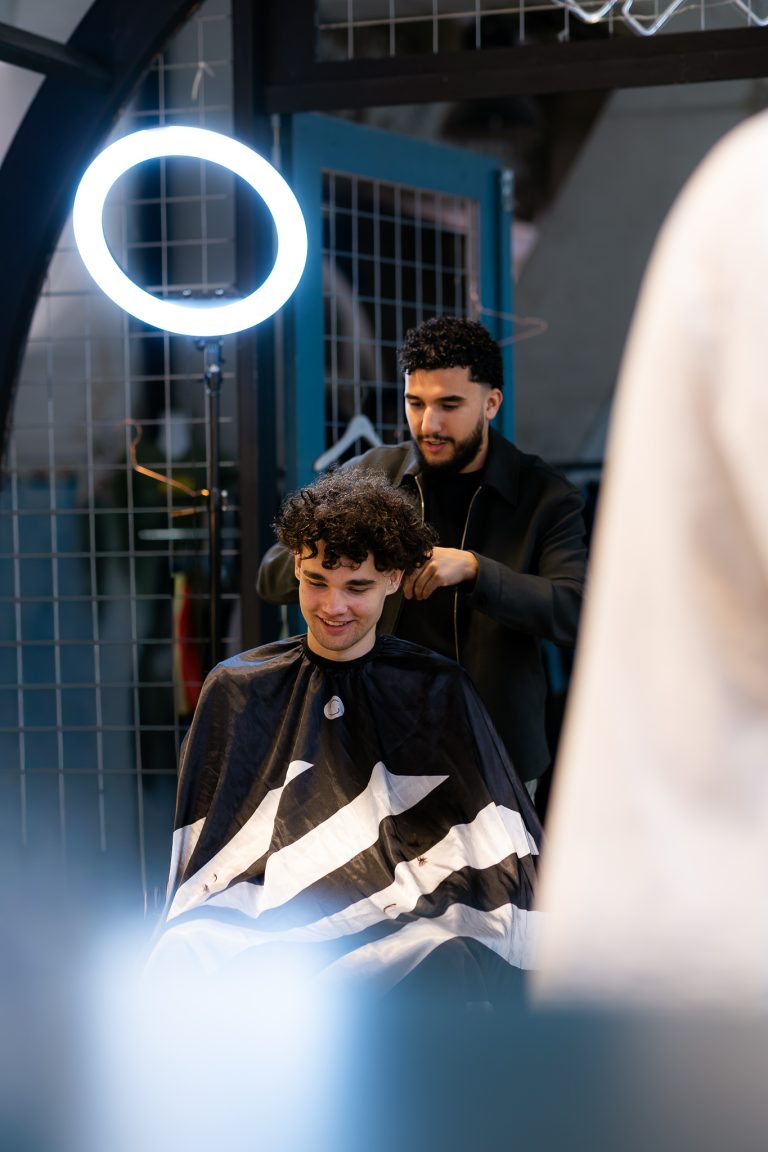 Barbier knipt het krullende haar van een klant die glimlachend in de stoel zit