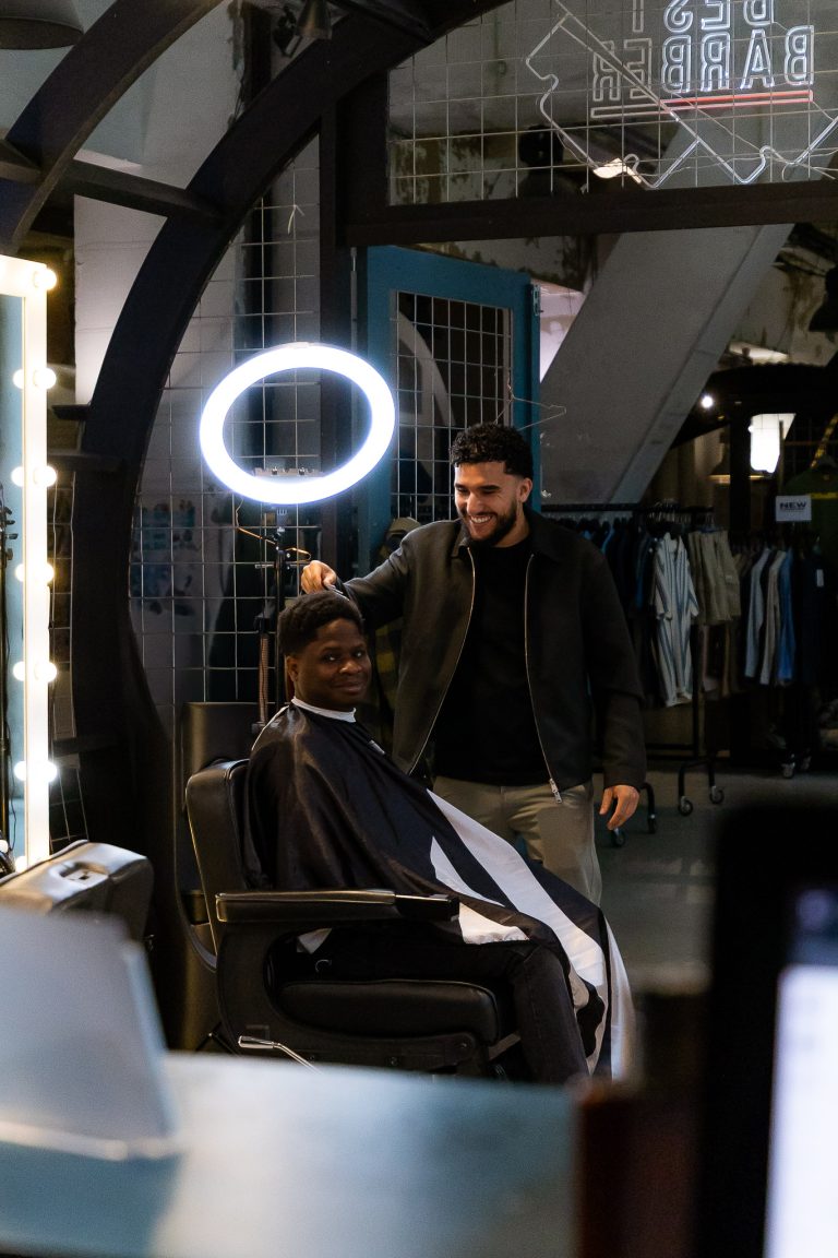 Klant met kort kroeshaar in de barberstoel terwijl de barbier het kapsel afwerkt